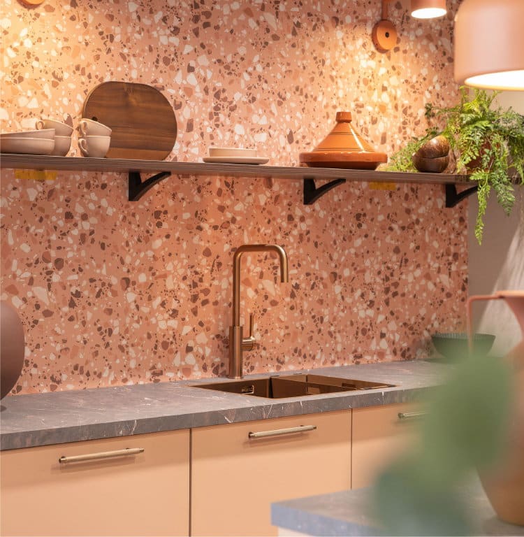 Keuken kleuren 2027: oranje-bruin terrazzo wandpanelen en koperen kraan, spoelbak en messing handgreepjes